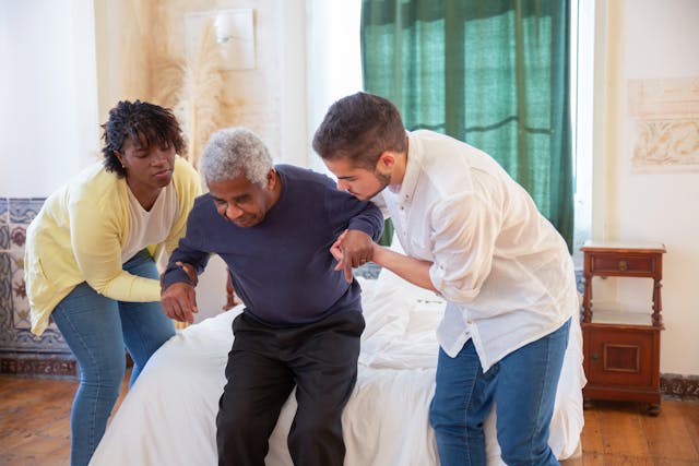 Man and a Woman Assisting an Elderly Man in Standing